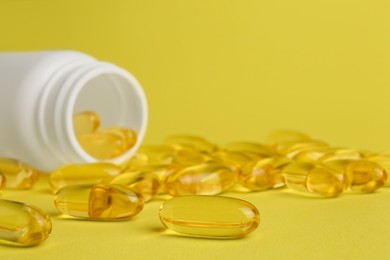 Photo of Open medicine bottle with scattered pills on yellow background, closeup