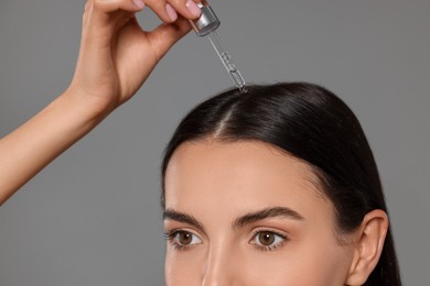 Photo of Beautiful woman applying hair serum on grey background, closeup. Cosmetic product