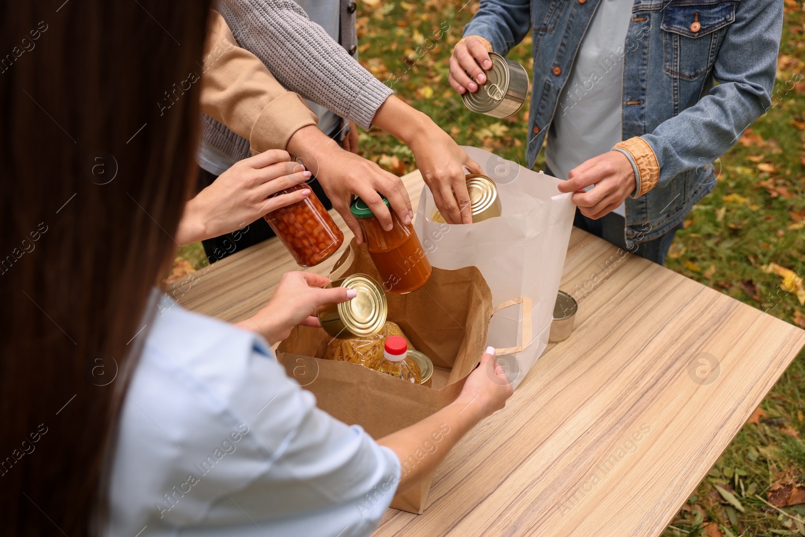 Photo of Group of volunteers packing food products at table outdoors, closeup