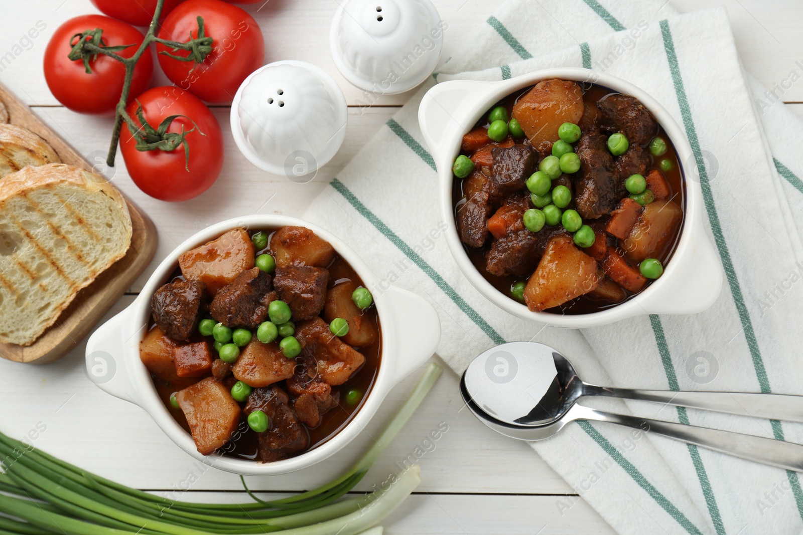 Photo of Delicious beef stew with carrots, peas and potatoes served on white wooden table, flat lay