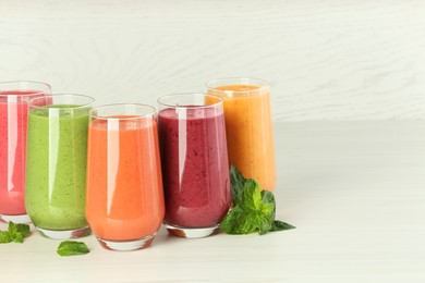 Photo of Colorful fruit smoothies and fresh mint on table against white wooden wall. Space for text