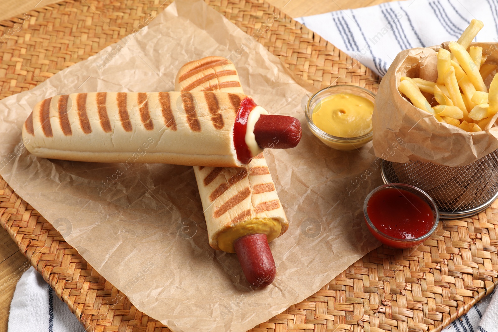 Photo of Delicious french hot dogs, fries and dip sauce on wicker mat