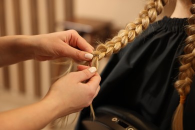 Photo of Professional hairdresser braiding girl's hair in beauty salon, closeup