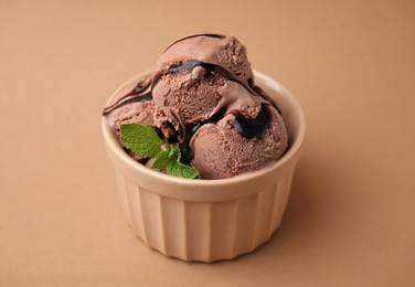 Bowl of tasty chocolate ice cream with mint on beige background, closeup