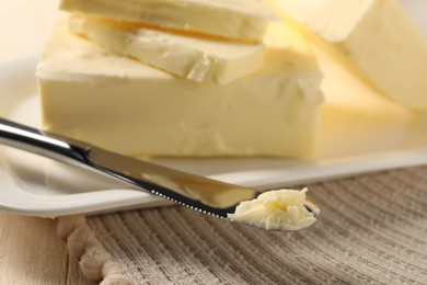 Tasty butter and knife on wooden table, closeup