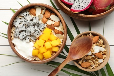 Photo of Bowl of granola with pitahaya, mango, almonds and yogurt on white wooden table, flat lay