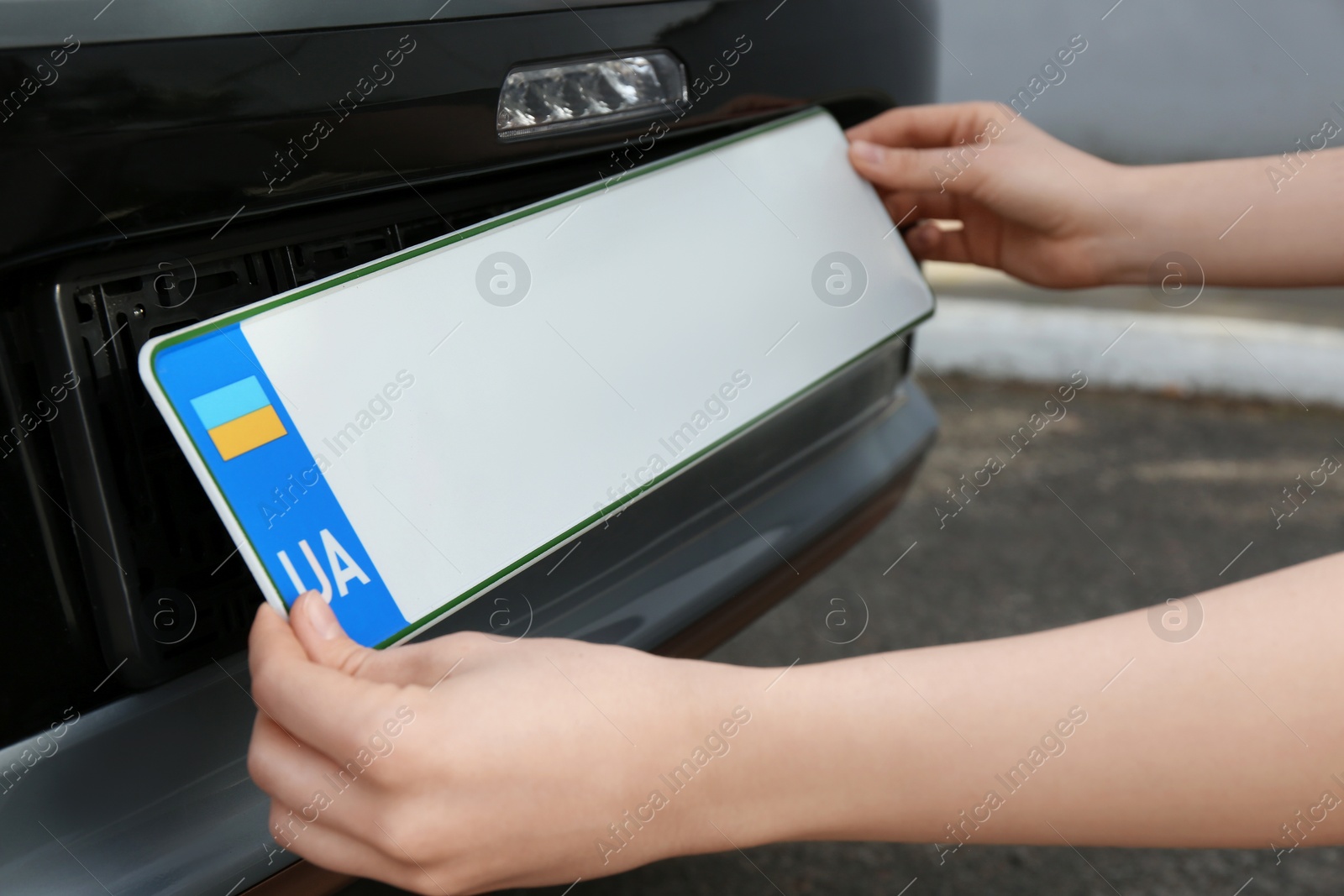 Photo of Woman installing vehicle registration plate outdoors, closeup