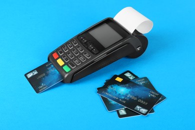 Photo of New modern payment terminal and credit cards on light blue background