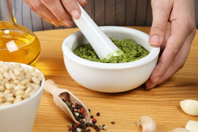 Photo of Woman mixing pesto sauce with pestle in mortar at table, closeup