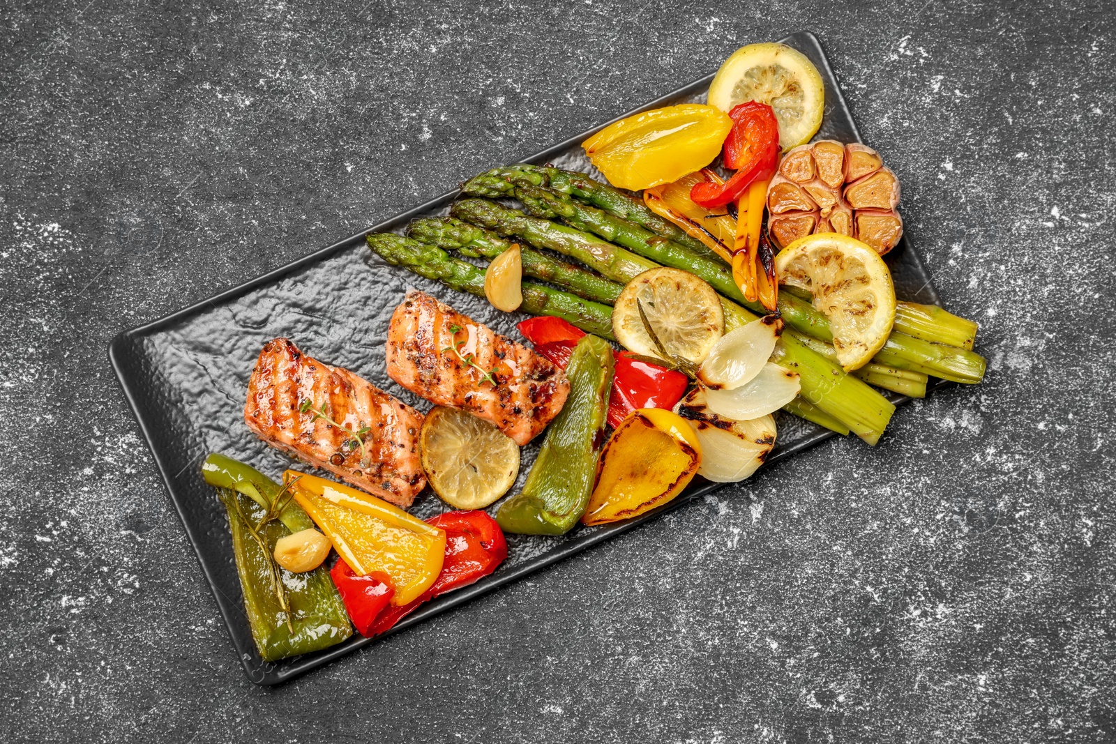 Photo of Tasty grilled salmon with lemon and vegetables on black table, top view