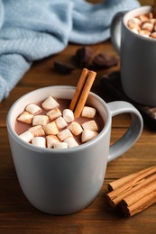 Delicious hot drink with cinnamon and marshmallows on wooden table