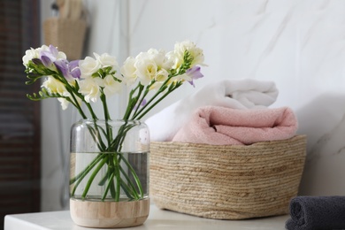 Photo of Beautiful freesia flowers and basket of towels on countertop in bathroom