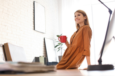 Young woman with cup of drink relaxing in office during break