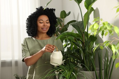 Photo of Happy woman watering beautiful potted houseplants indoors