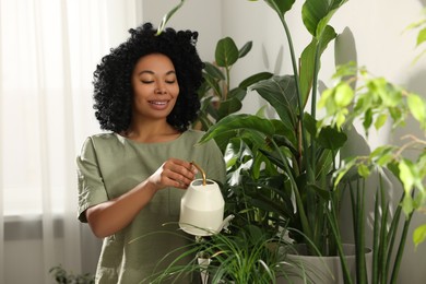 Happy woman watering beautiful potted houseplants indoors