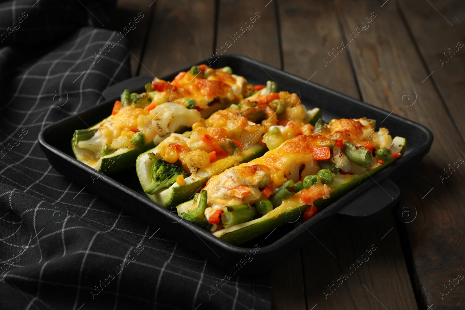 Photo of Baking dish with stuffed zucchinis served on wooden table, closeup