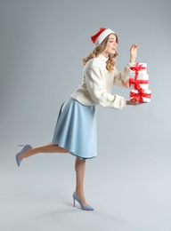 Photo of Beautiful young woman in Santa hat with Christmas presents on light grey background