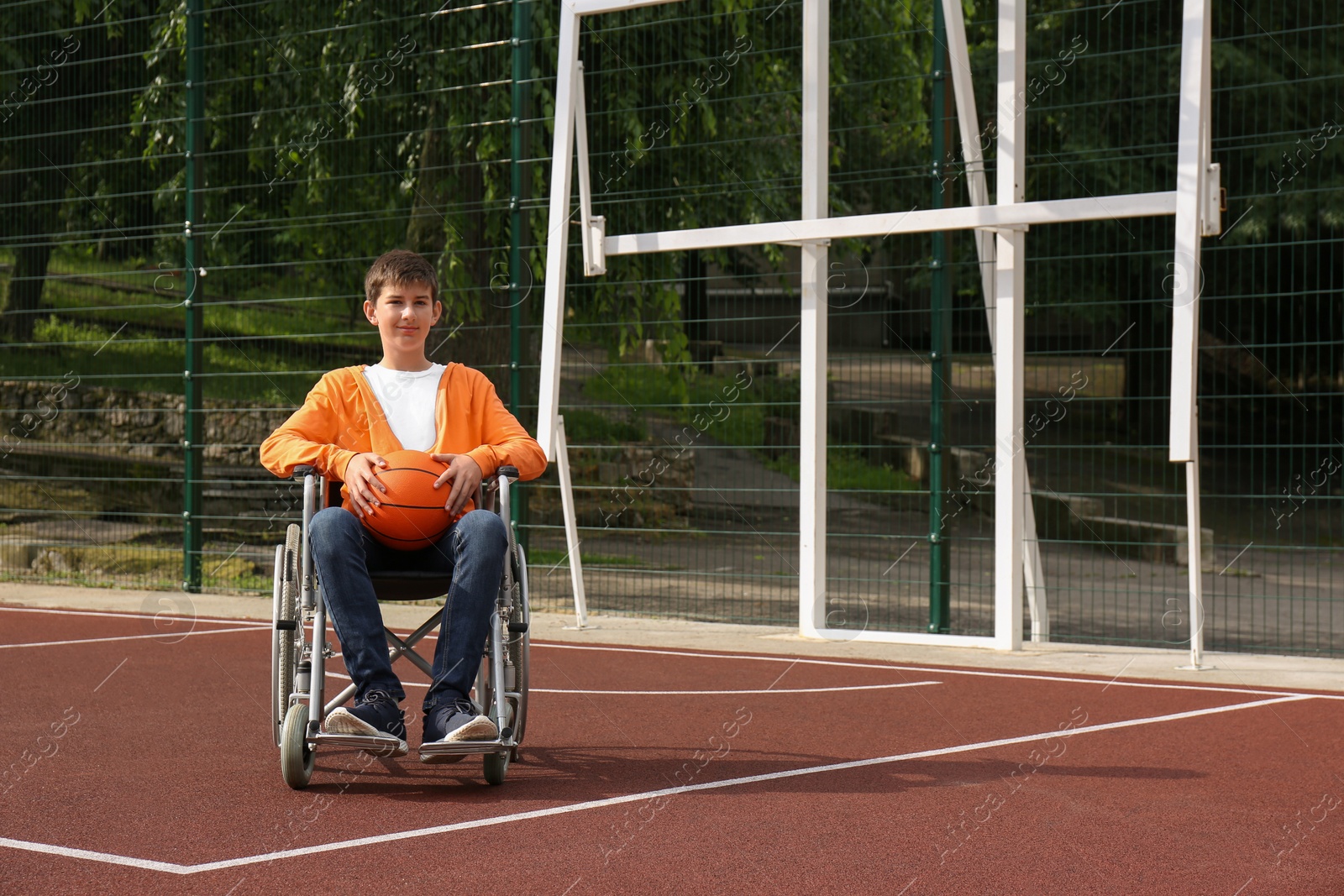 Photo of Disabled teenage boy in wheelchair with basketball ball at outdoor court