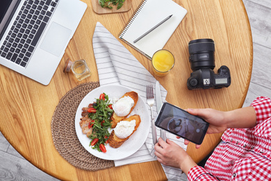 Photo of Food blogger taking photo of her lunch at wooden table, above view