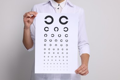 Photo of Ophthalmologist with vision test chart on light background, closeup