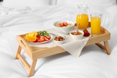 Photo of Tasty breakfast served in bed. Oatmeal, juice, fruits, almonds and honey on wooden tray