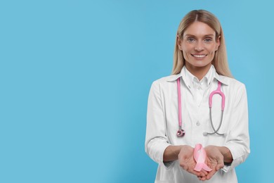 Doctor with stethoscope holding pink ribbon on light blue background, space for text. Breast cancer awareness