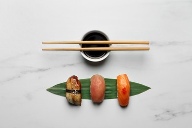 Delicious nigiri sushi, chopsticks and soy sauce on white marble table, flat lay