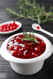 Photo of Fresh cranberry sauce in bowl and rosemary on black wooden table, closeup