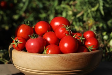 Photo of Bowl of ripe tomatoes on wooden table outdoors, closeup