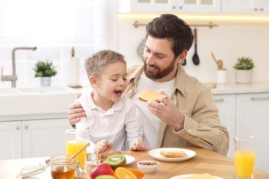 Father and his cute little son having breakfast at table in kitchen