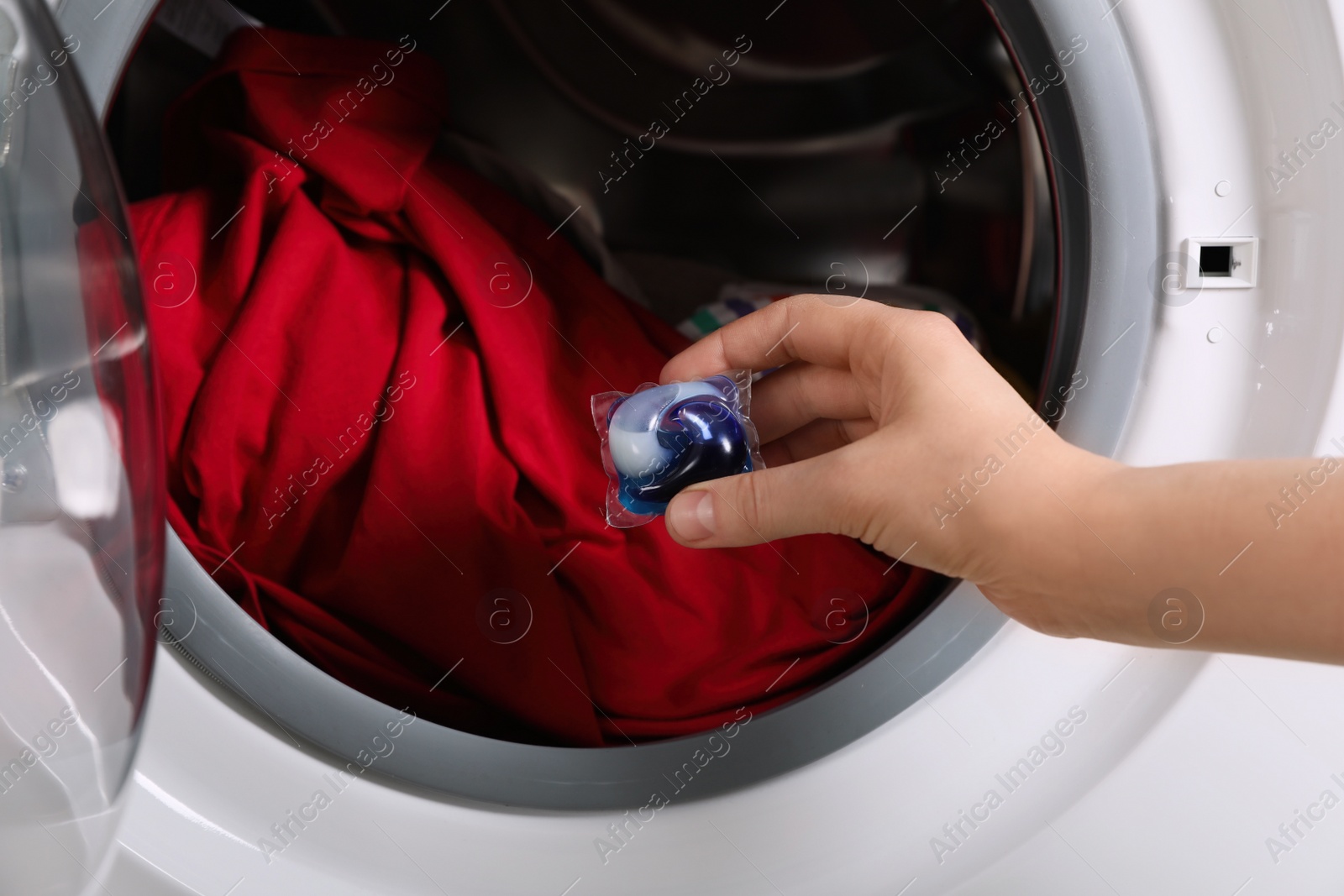 Photo of Woman putting laundry detergent capsule into washing machine, closeup