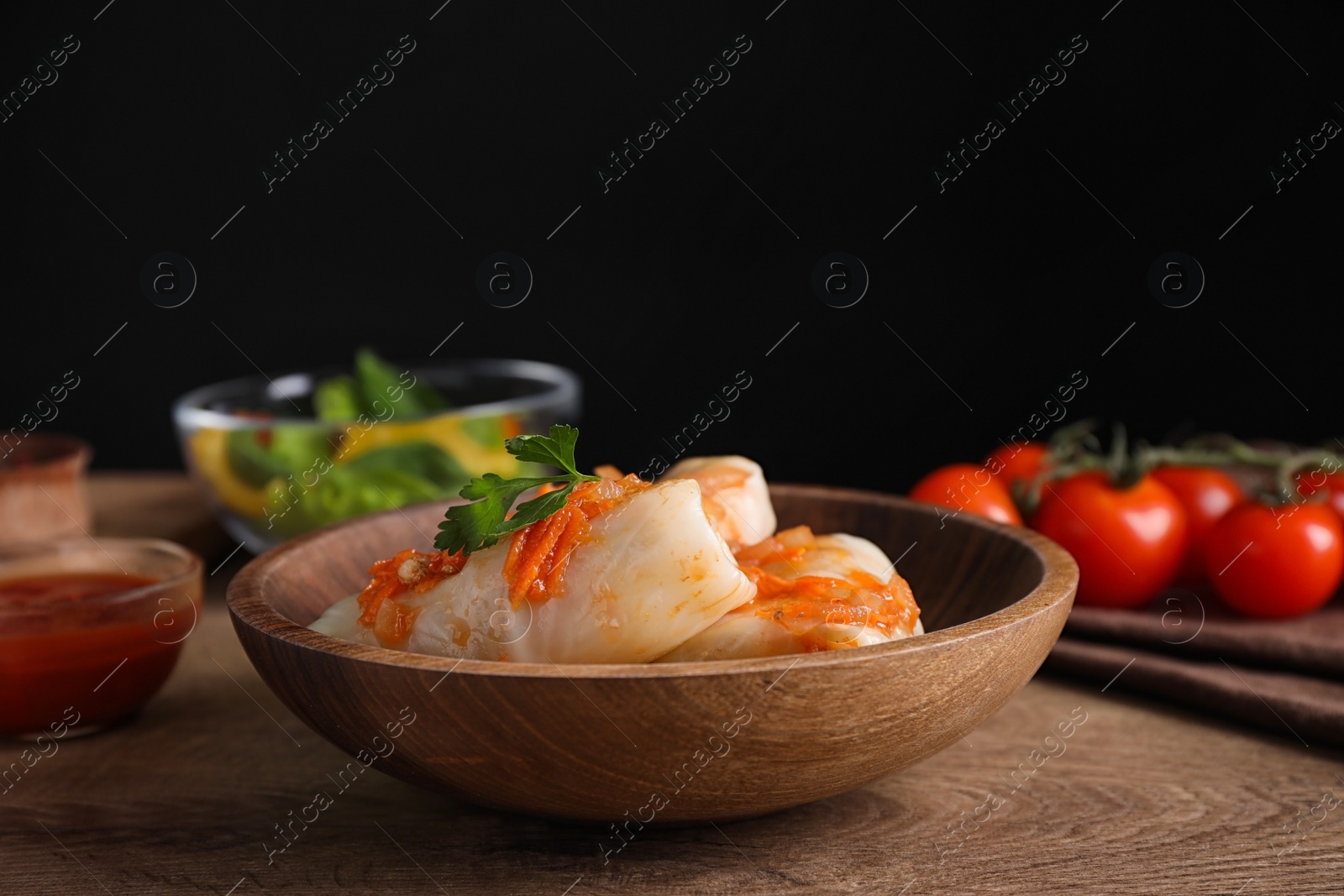 Photo of Delicious cabbage rolls served on wooden table against black background