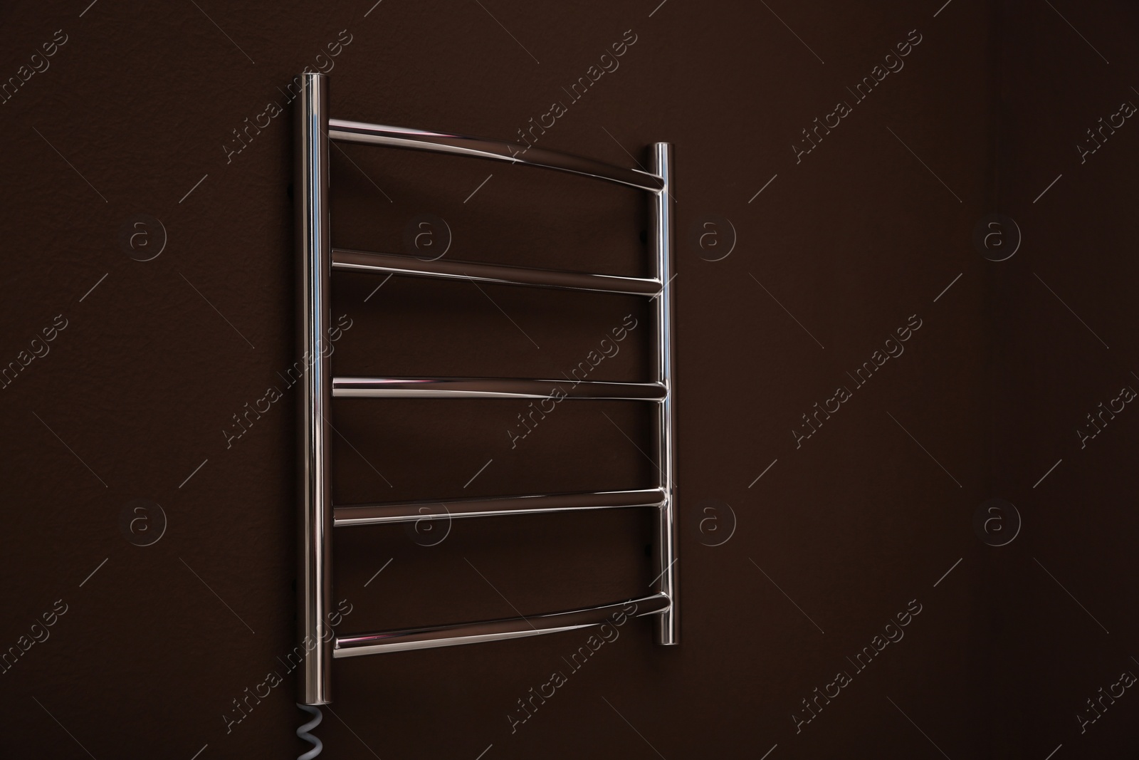 Photo of Modern heated towel rail on brown wall. Space for text