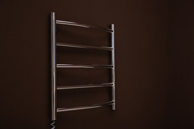 Photo of Modern heated towel rail on brown wall. Space for text