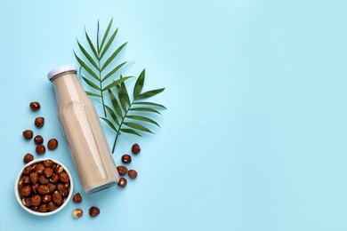 Photo of Bottle of vegan milk and hazelnuts on light blue background, flat lay. Space for text