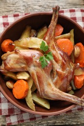 Photo of Tasty cooked rabbit with vegetables in bowl on wooden table, top view