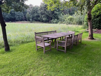 Photo of Wooden table with bench and chairs in garden. Landscape design
