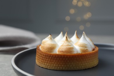 Tartlet with meringue on grey table against blurred festive lights, closeup and space for text. Delicious dessert