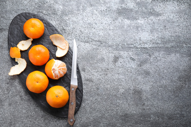 Photo of Fresh ripe tangerines and knife on grey table, top view. Space for text