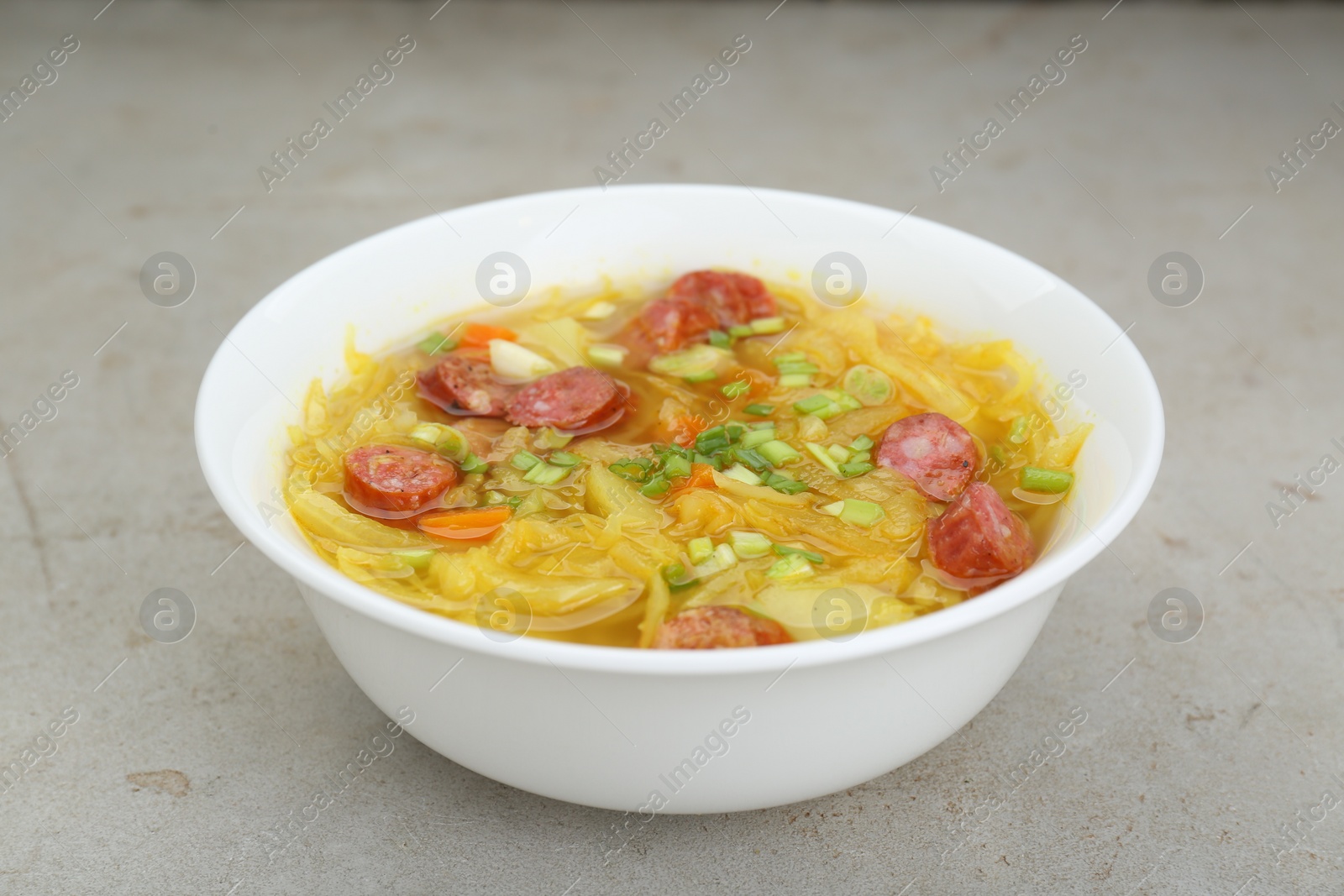 Photo of Delicious sauerkraut soup with smoked sausages and green onion on light grey table