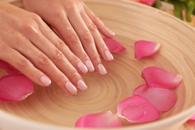 Photo of Woman soaking her hands in bowl of water and petals, closeup with space for text. Spa treatment