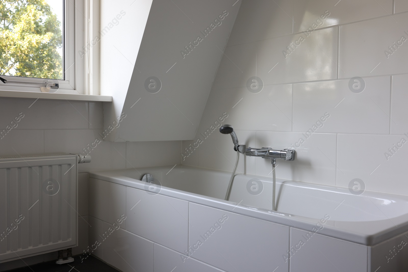 Photo of Clean tub with showerhead and tap in white bathroom. Interior design