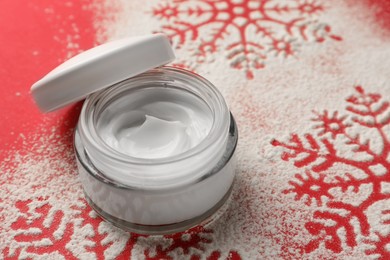 Photo of Winter skin care. Hand cream near snowflake silhouettes made with artificial snow on red background, closeup