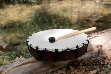 Photo of Modern drum and drumstick on stump outdoors. Percussion musical instrument