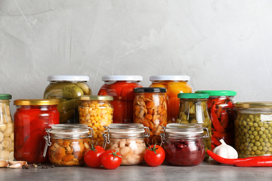 Glass jars with different pickled vegetables on grey table