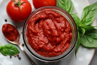 Photo of Jar of tasty tomato paste and ingredients on plate, top view