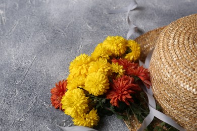 Photo of Bright chrysanthemum flowers and wicker hat on grey textured table, space for text