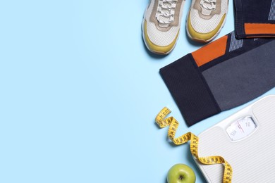 Flat lay composition with sportswear and floor scales on light blue background. Space for text