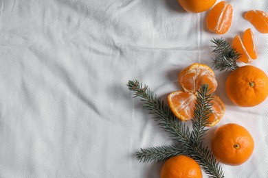 Delicious ripe tangerines and fir branches on white bedsheet, flat lay. Space for text