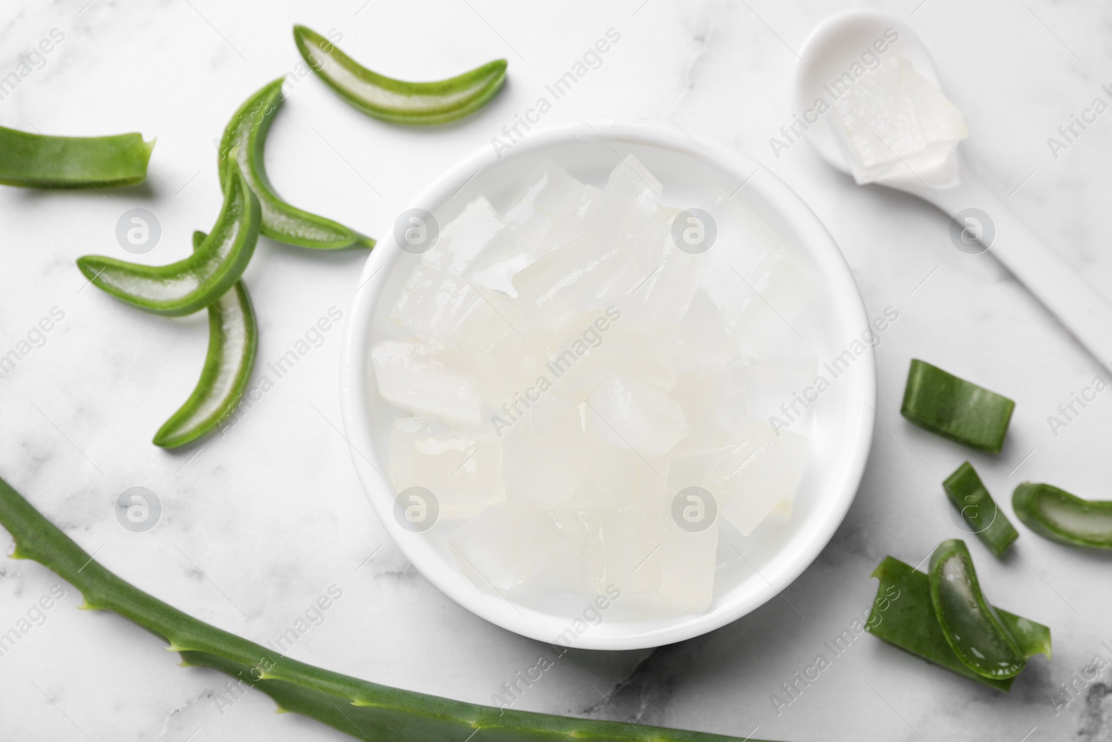 Photo of Aloe vera gel and slices of plant on white marble table, flat lay